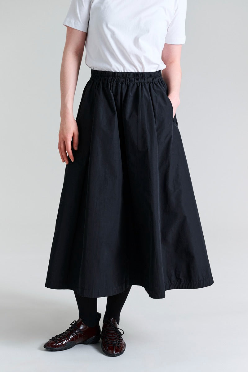 Person wearing a black skirt and white shirt on a plain background