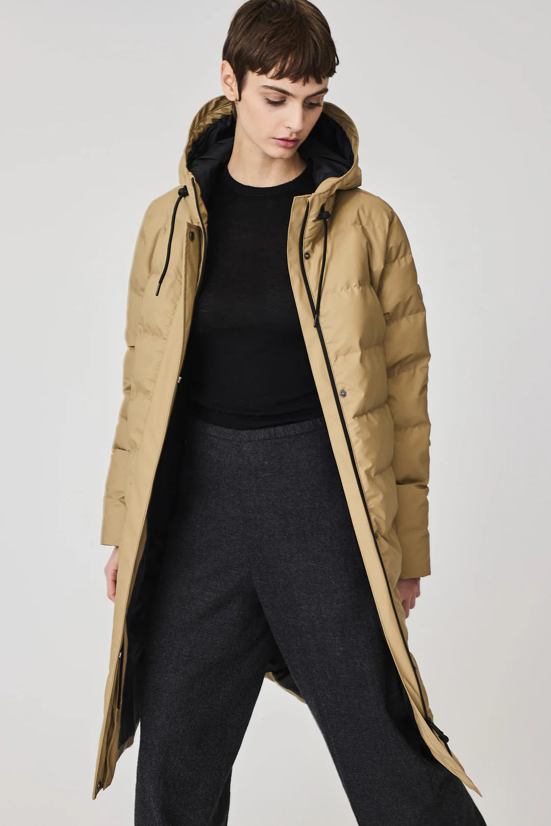 Woman wearing a long beige puffer coat on a white background