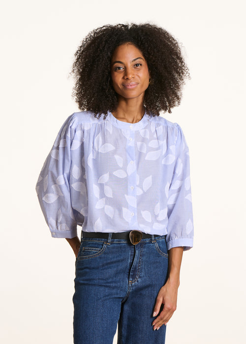 Woman wearing a light blue patterned blouse and blue jeans on a white background