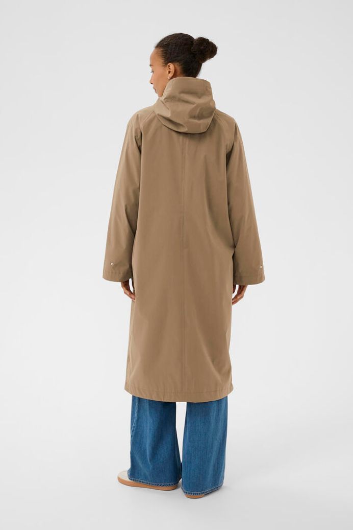 Person wearing a beige coat and blue pants on a white background