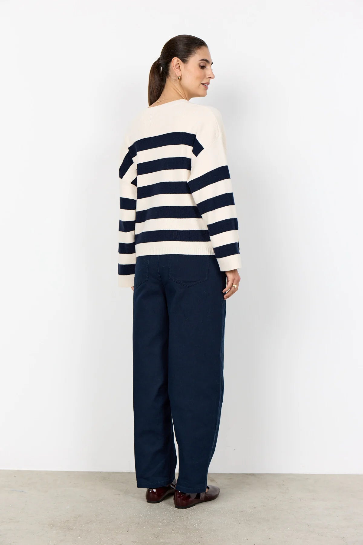 Person wearing a striped sweater and navy pants against a white background